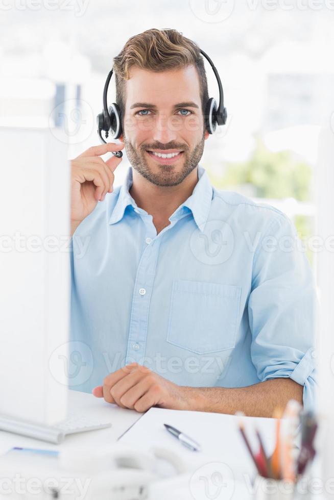 Porträt eines lässigen jungen Mannes mit Headset unter Verwendung des Computers foto