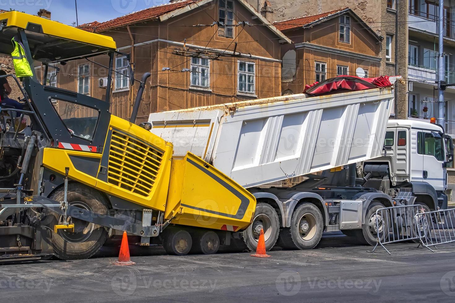 Ein LKW entlädt Asphalt in einer Asphaltmaschine. eine neue Straße machen foto