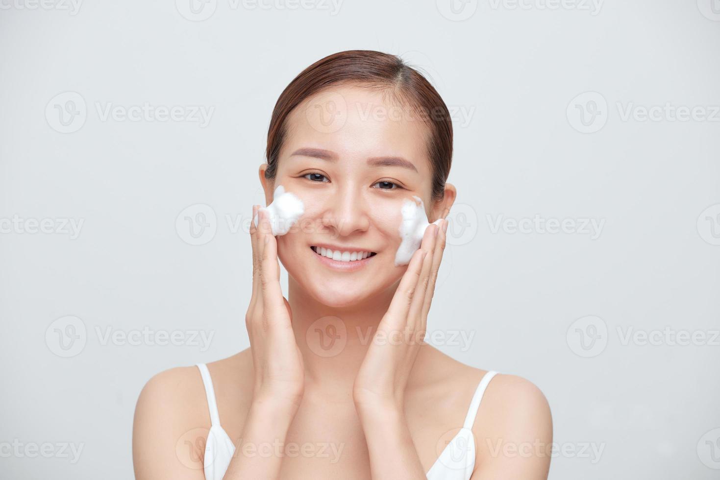 Porträt einer jungen asiatischen Frau, die schäumende Reinigungsmittel vor weißem Hintergrund anwendet. foto