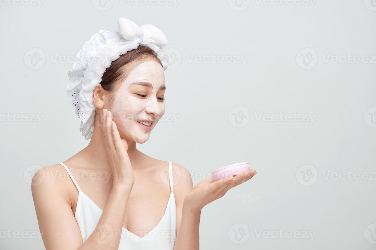 junge asiatische frau, die gesichtslehmmaske gegen weißen hintergrund anwendet. foto