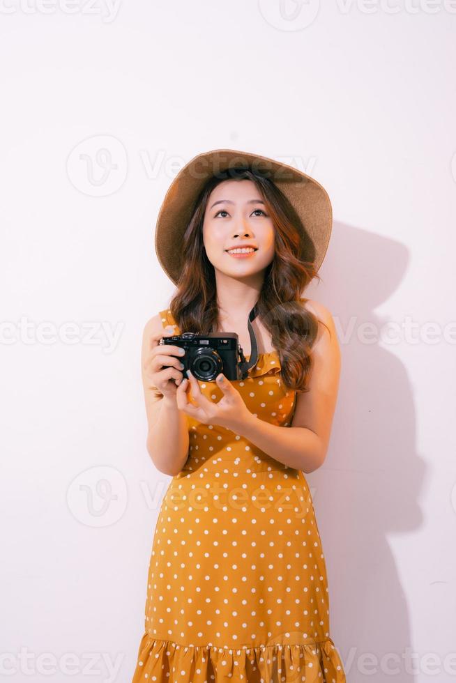 stilvolle lächelnde frau, die mit retro-kamera auf rosa hintergrund aufwirft. foto