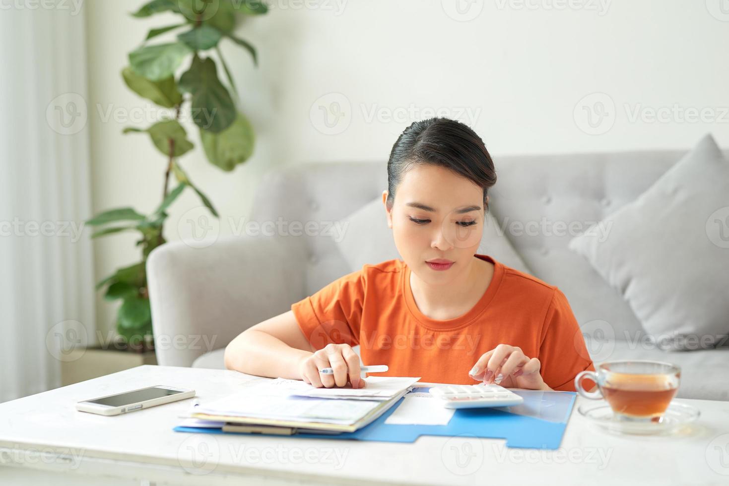 eine junge frau sitzt im wohnzimmer und schaut sich zu hause ihre rechnungen an foto