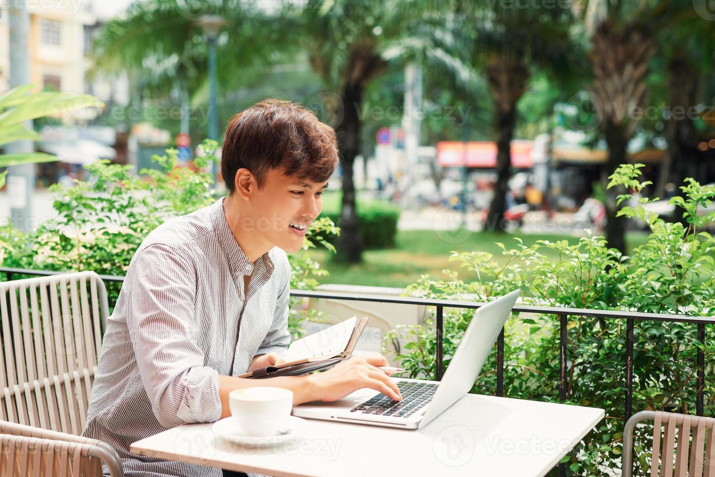 lächelnder junger mann, der laptop für arbeitsauftrag verwendet foto