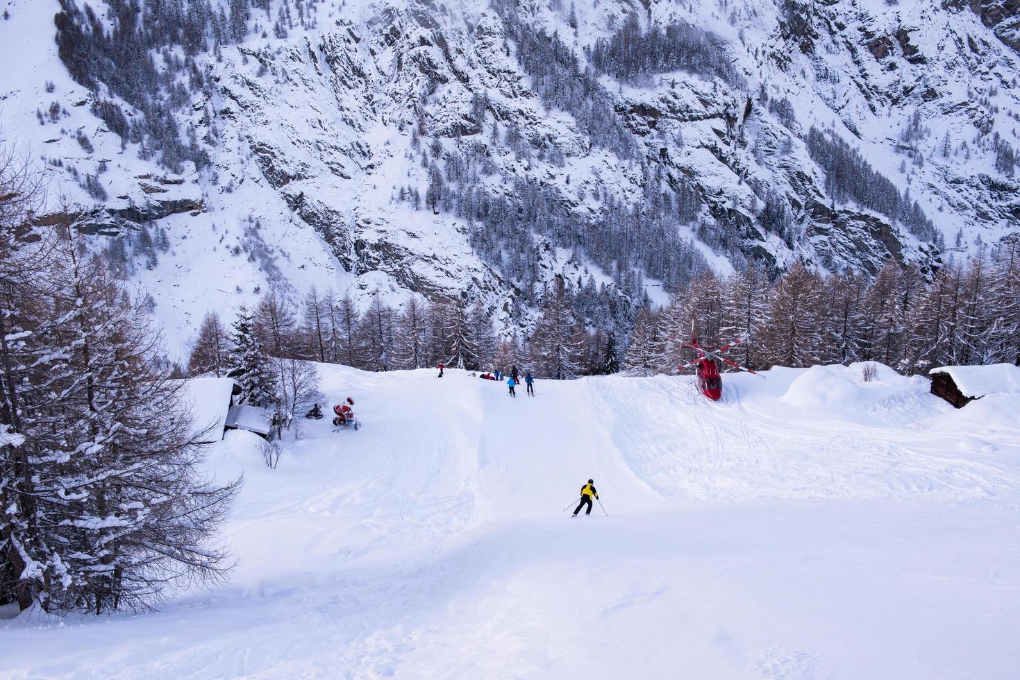 Rettungsteam mit einem roten Hubschrauber, der einen verletzten Skifahrer rettet foto