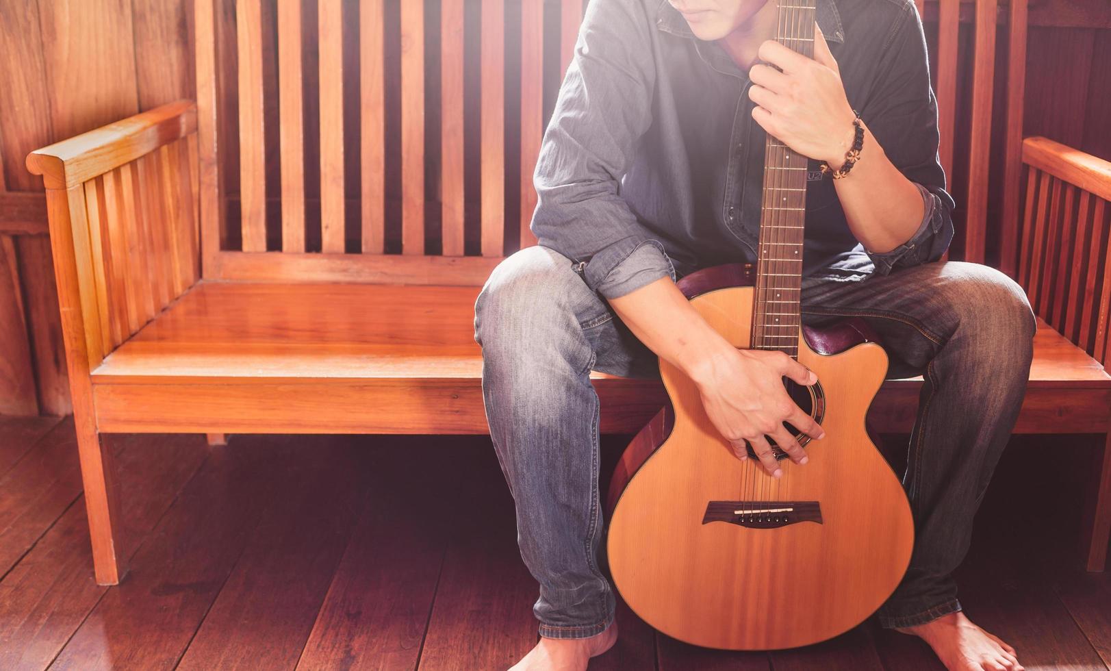 mann mit einer akustischen gitarre, die auf einem hölzernen sofa sitzt. musiker- und hipsterkonzept foto