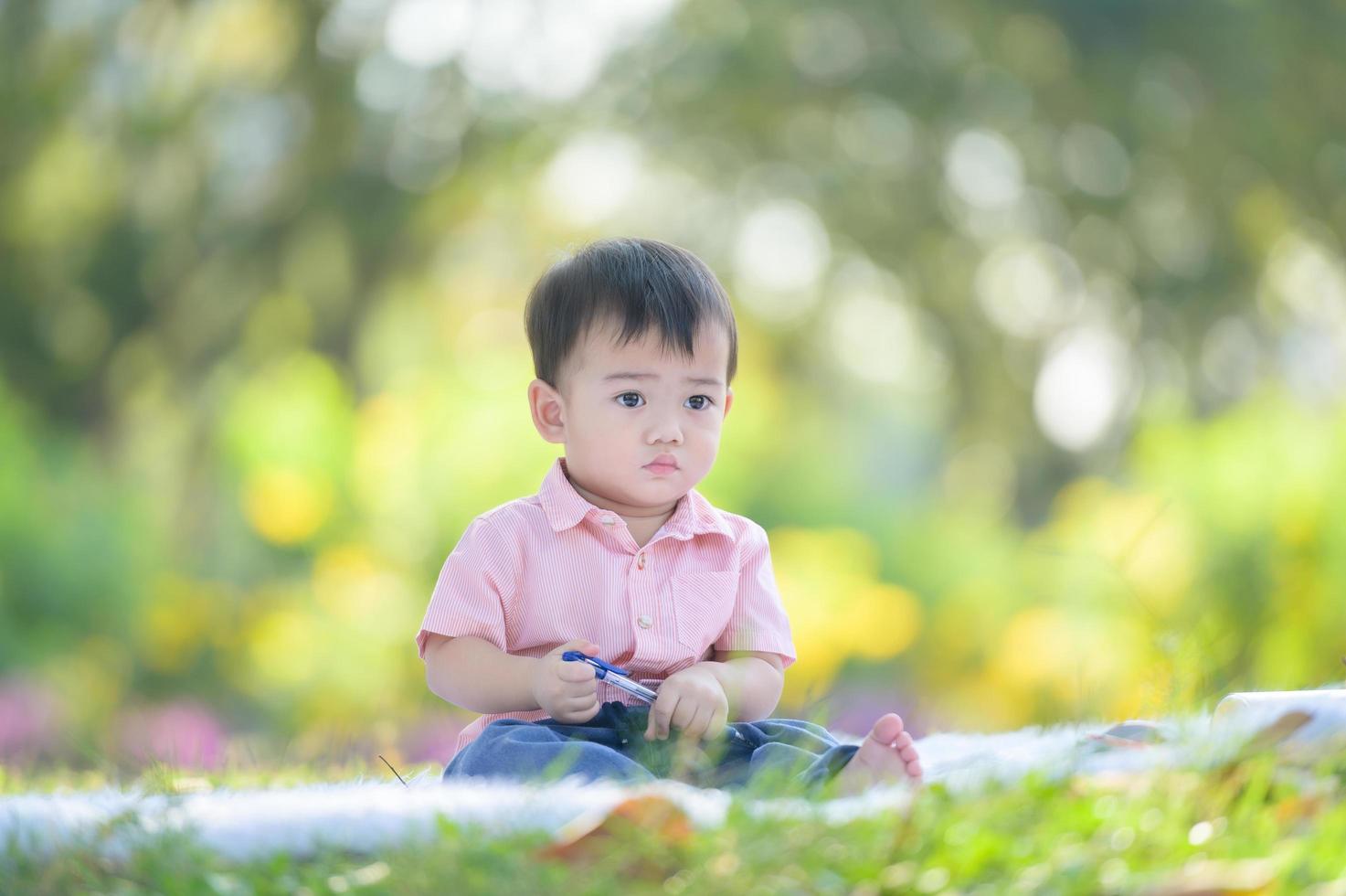 asiatischer junge, der auf dem teppich sitzt und einen stift hält, während er von außerhalb der schule im naturpark lernt foto