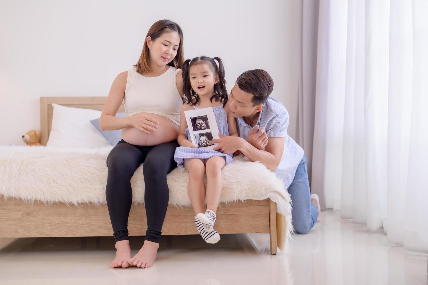 eine asiatische familie, eltern und töchter sehen sich einen ultraschallfilm eines kindes im bauch ihrer mutter an foto