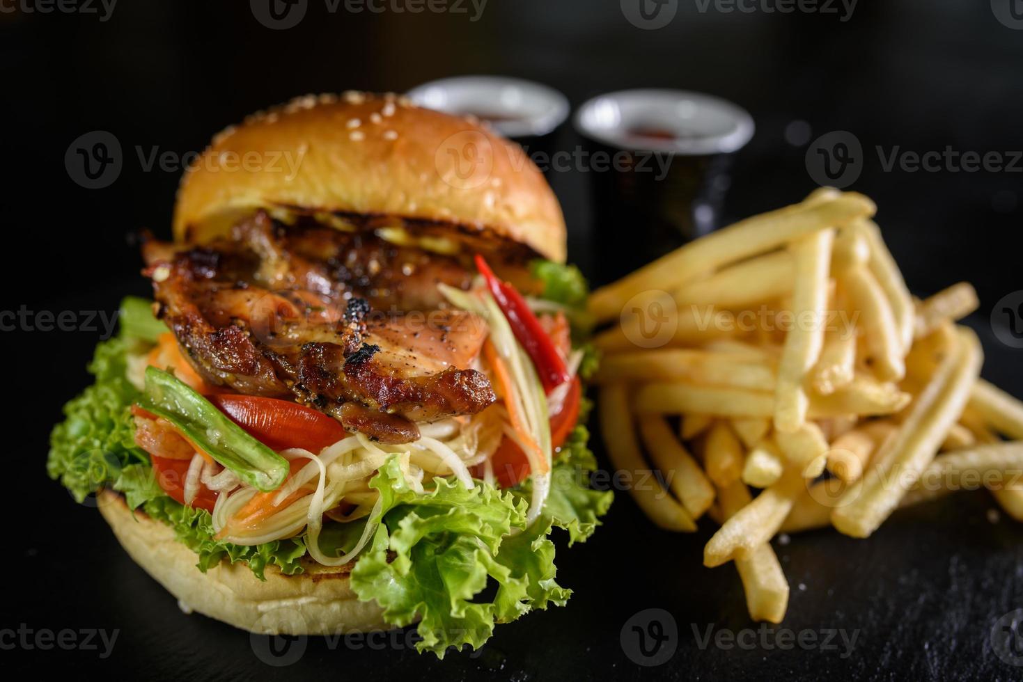 Köstlicher gegrillter Hühnerburger und Pommes auf schwarzem Holztischhintergrund foto