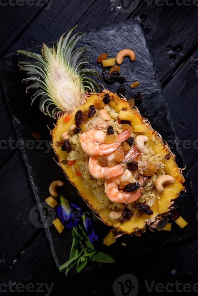 Gebratener Reis mit Meeresfrüchten, serviert mit Ananas auf einem schwarzen Holzboden foto