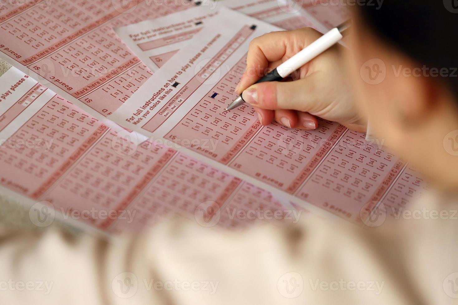 Lottoschein ausfüllen. Eine junge Frau spielt Lotto und träumt davon, den Jackpot zu gewinnen. weibliche Handmarkierungsnummer auf rotem Lottoschein foto