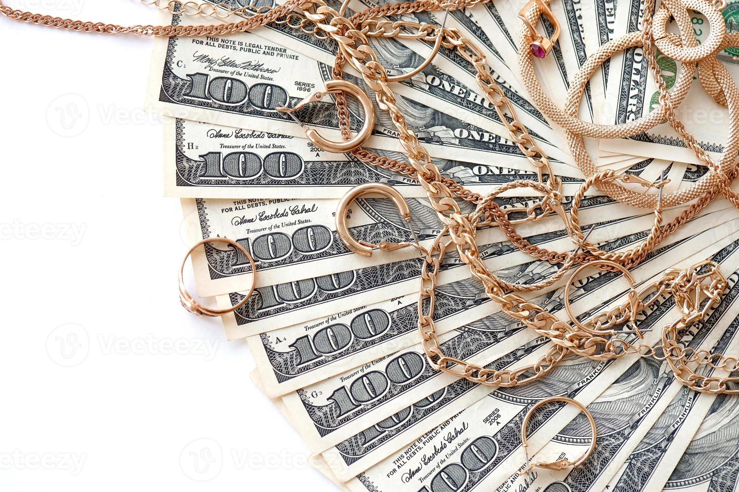 Viele teure goldene Schmuckringe, Ohrringe und Halsketten mit einer großen Menge US-Dollar-Scheine auf weißem Hintergrund. Pfandhaus oder Juweliergeschäft foto