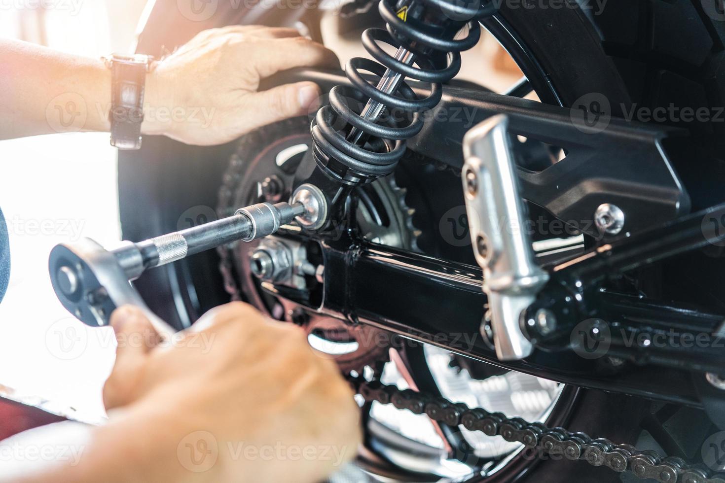 mechaniker, der einen schraubenschlüssel und eine buchse verwendet, um die einstellbare hintere motorradaufhängung zu entfernen und zu ersetzen, die in der garagenwartung arbeitet, das motorradkonzept repariert. selektiv foto