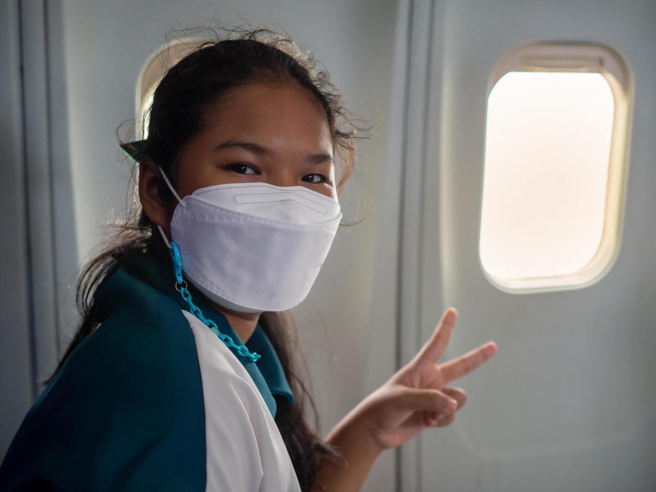 Eine Frau mit Maske sitzt am Fenster eines Flugzeugs. foto