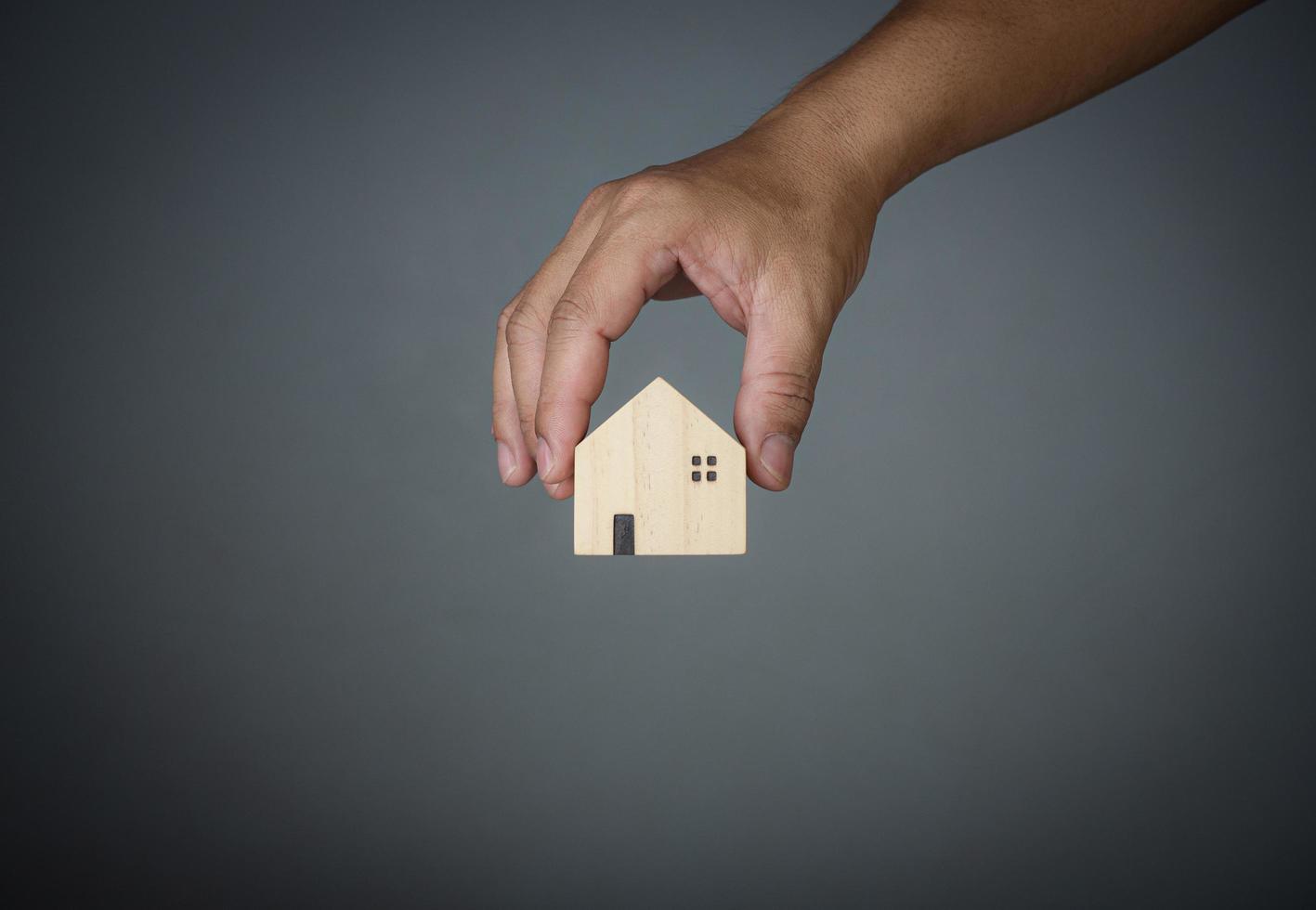 Konzept des Verkaufs eines Hauses. Eine Hand hält ein Musterhaus auf grauem Hintergrund. immobilienmakler bieten haus, sachversicherung und sicherheit, bezahlbare wohnkonzepte, verkäufer person. foto