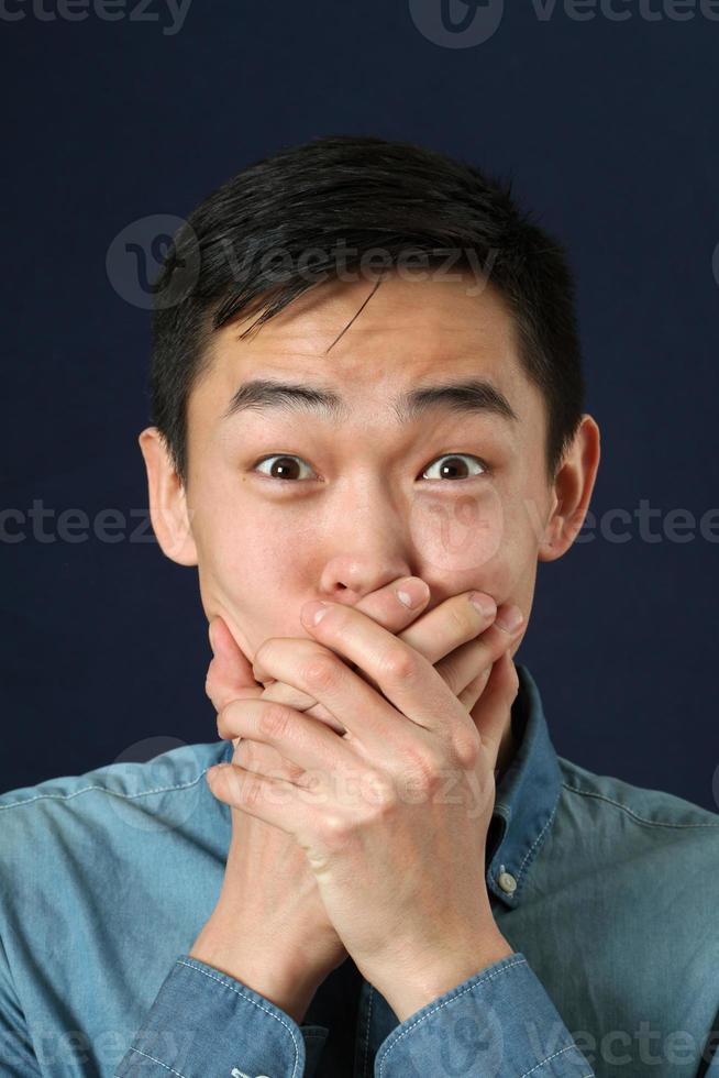 überraschter junger asiatischer Mann, der seinen Mund mit Handflächen bedeckt foto