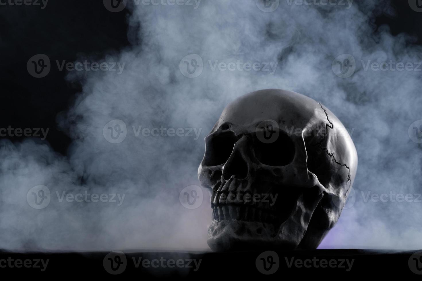 Halloween menschlicher Schädel auf einem alten Holztisch auf schwarzem Hintergrund. form des schädelknochens für totenkopf auf dem halloween-festival, das horror, böse zahnangst und gruselig mit nebelrauch zeigt, kopierraum foto