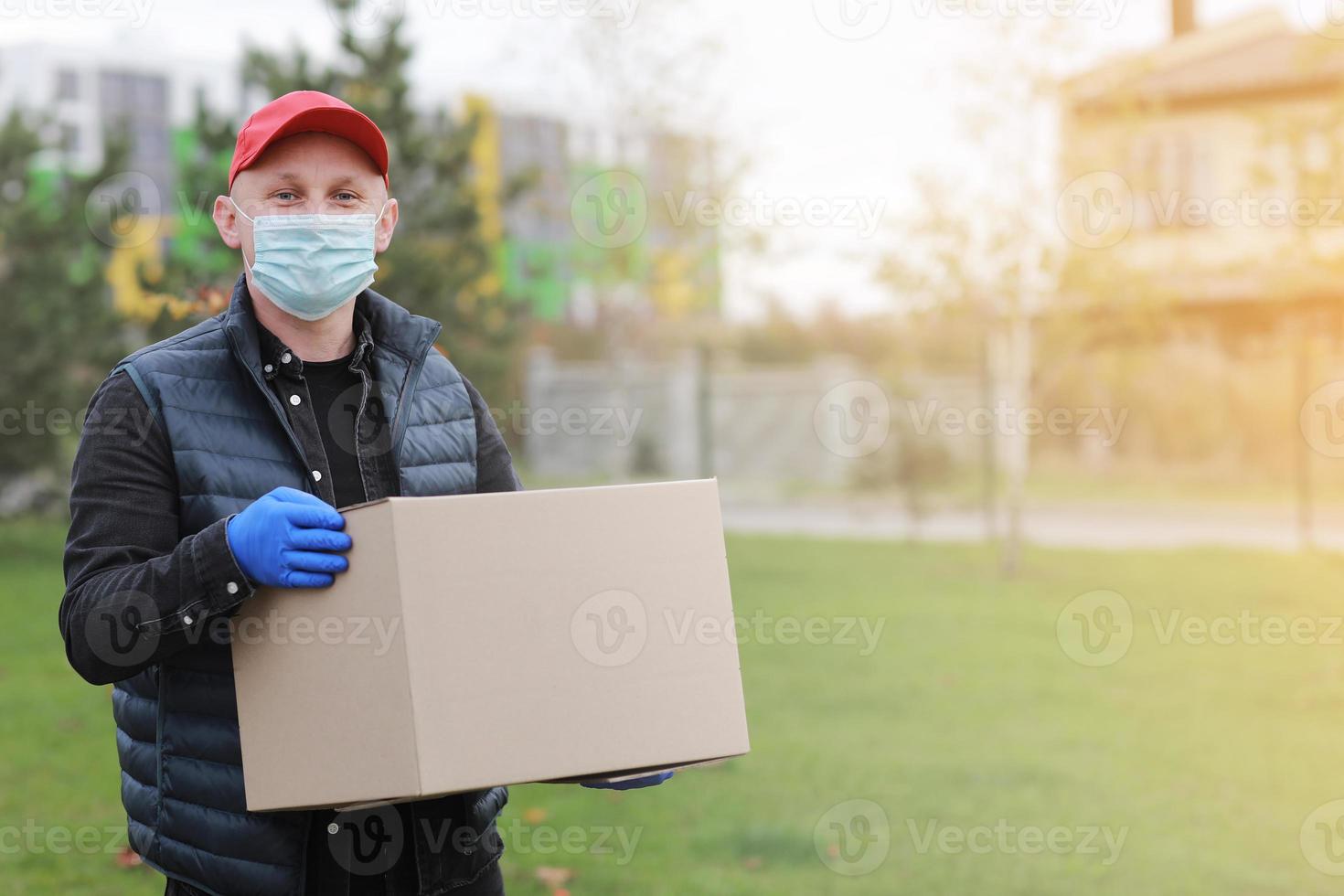 lieferbote mit roter kappe, medizinischer gesichtsmaske, handschuhe halten leere pappschachtel im freien. Service-Coronavirus. Online Einkaufen. Attrappe, Lehrmodell, Simulation. foto