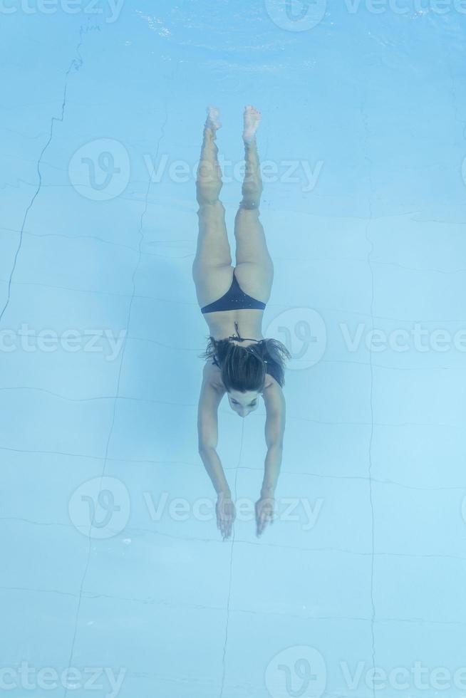 Drohnenblick auf junge Frau, die im blauen Swimmingpool taucht foto