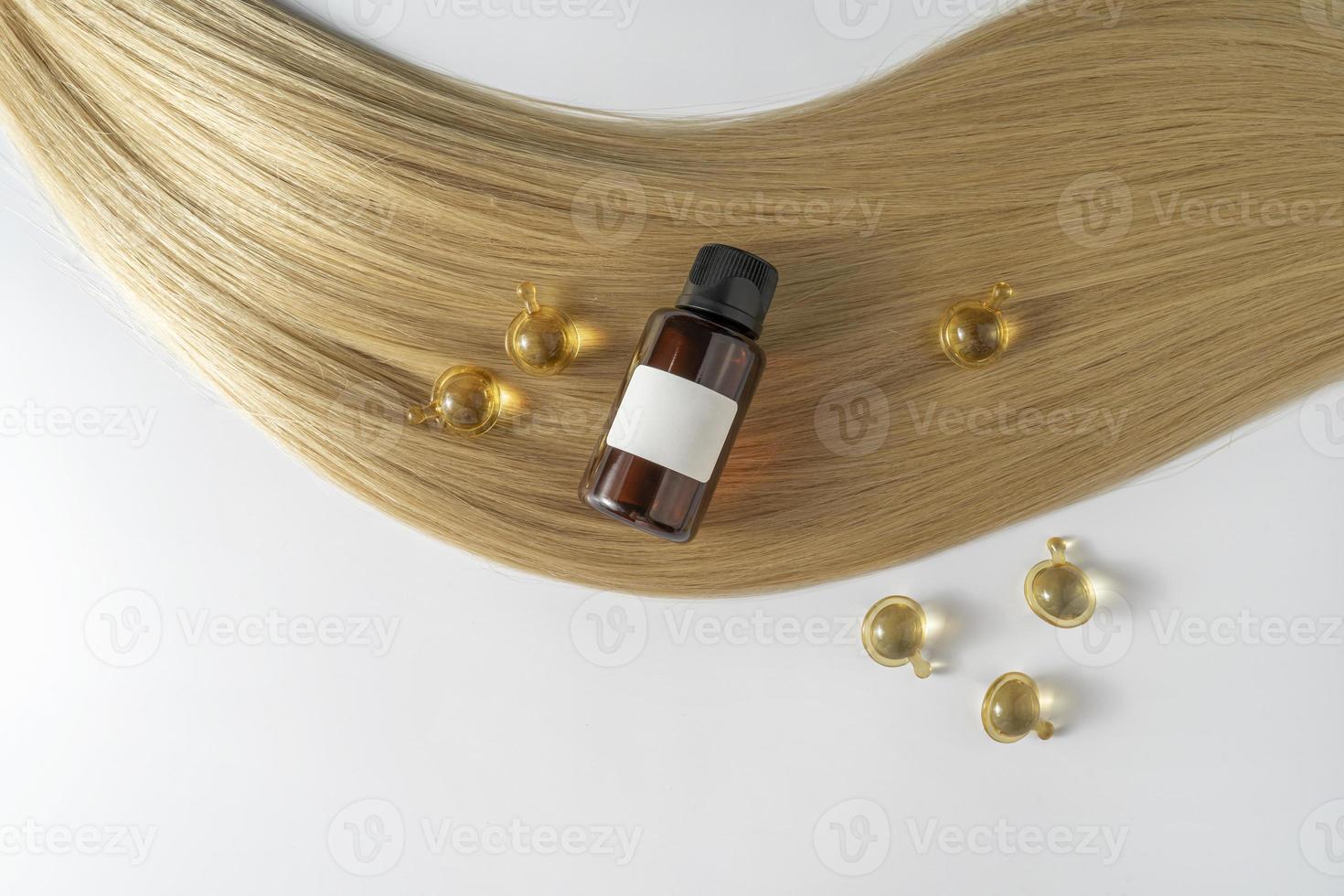 Ein Haarpflegeöl oder Serum in einer braunen Tropfflasche und goldene Kapseln, die auf einer blonden Haarsträhne liegen, Produktmarketing-Mockup foto