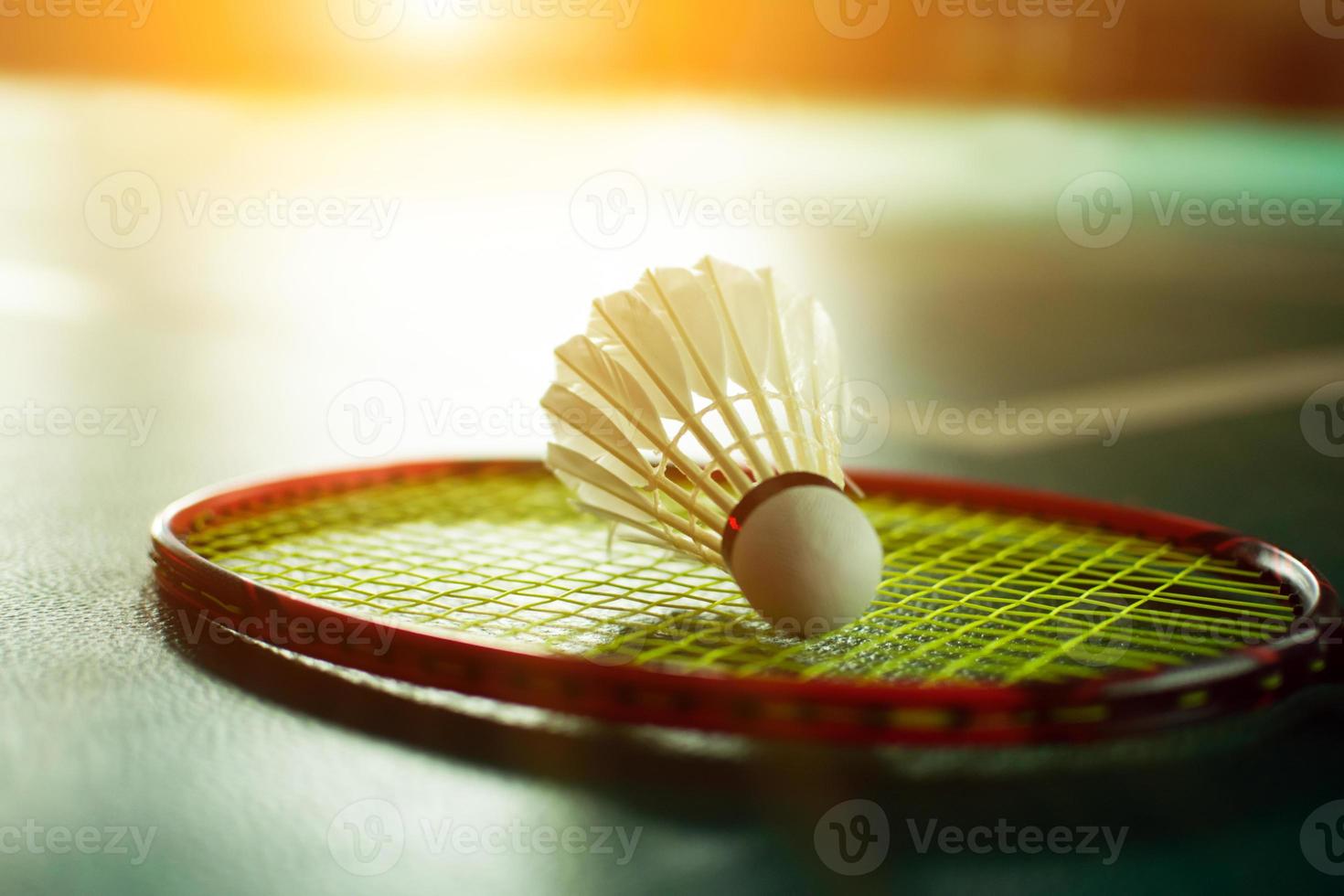 Cremeweißer Badmintonfederball und Schläger mit Neonlichtschattierung auf grünem Boden im Indoor-Badmintonplatz, verschwommener Badmintonhintergrund, Kopierraum. foto