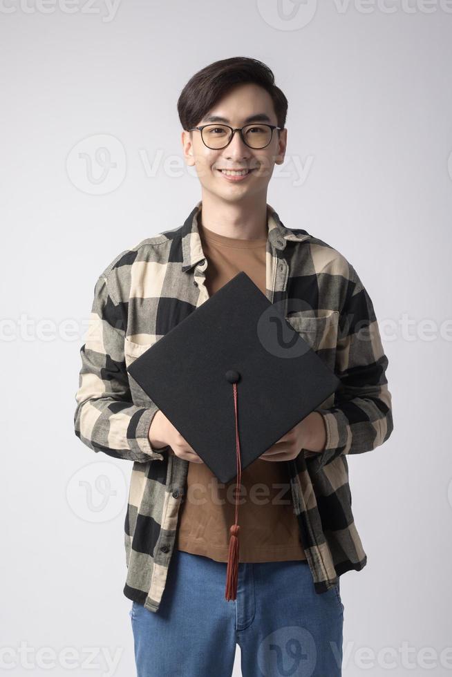 junger lächelnder mann, der abschlusshut, bildungs- und universitätskonzept hält foto