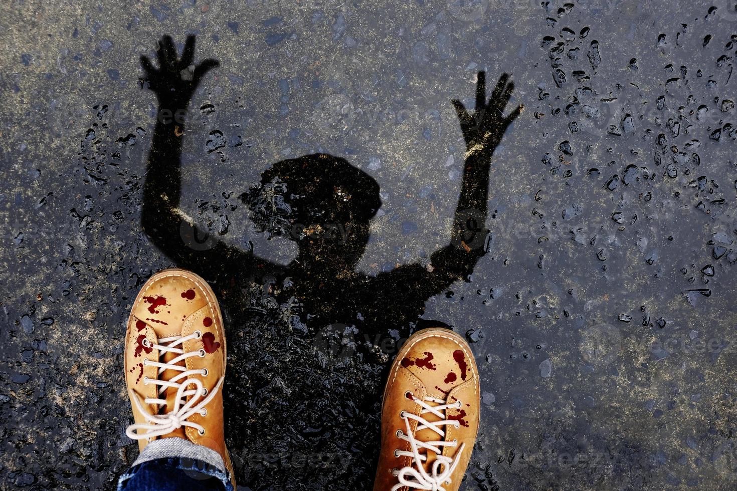 gruseliger zombiemann mit tropfendem blut auf schuhen hebt gruselige hand. Präsentieren Sie sich durch Reflexionsschatten auf dem Boden, nachdem der Regen für den Halloween-Tag oder die Horrorgeschichte aufgehört hat foto