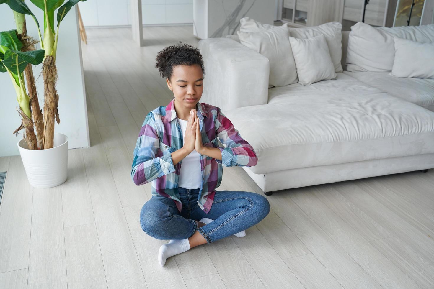 ruhiges Mischlingsmädchen, das zu Hause Yoga in Lotus-Pose auf dem Boden praktiziert. gesunder Lebensstil, Meditation foto