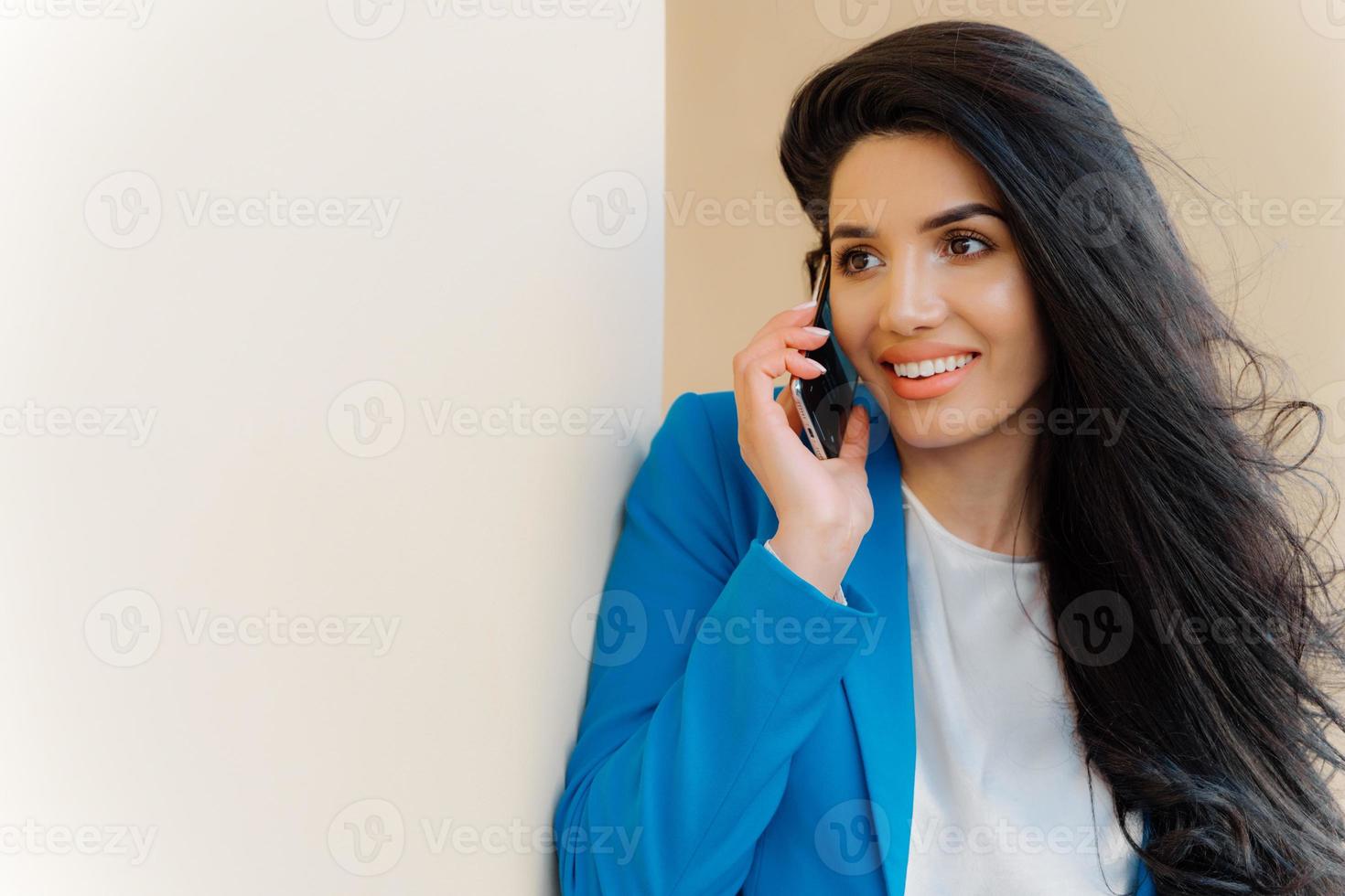 Foto einer brünetten Frau mit angenehmem Aussehen, luxuriösem Haar, Gesprächen am Handy, gekleidet in formelle Kleidung, arrangiert ein Geschäftstreffen mit dem Partner. menschen, technik, kommunikationskonzept