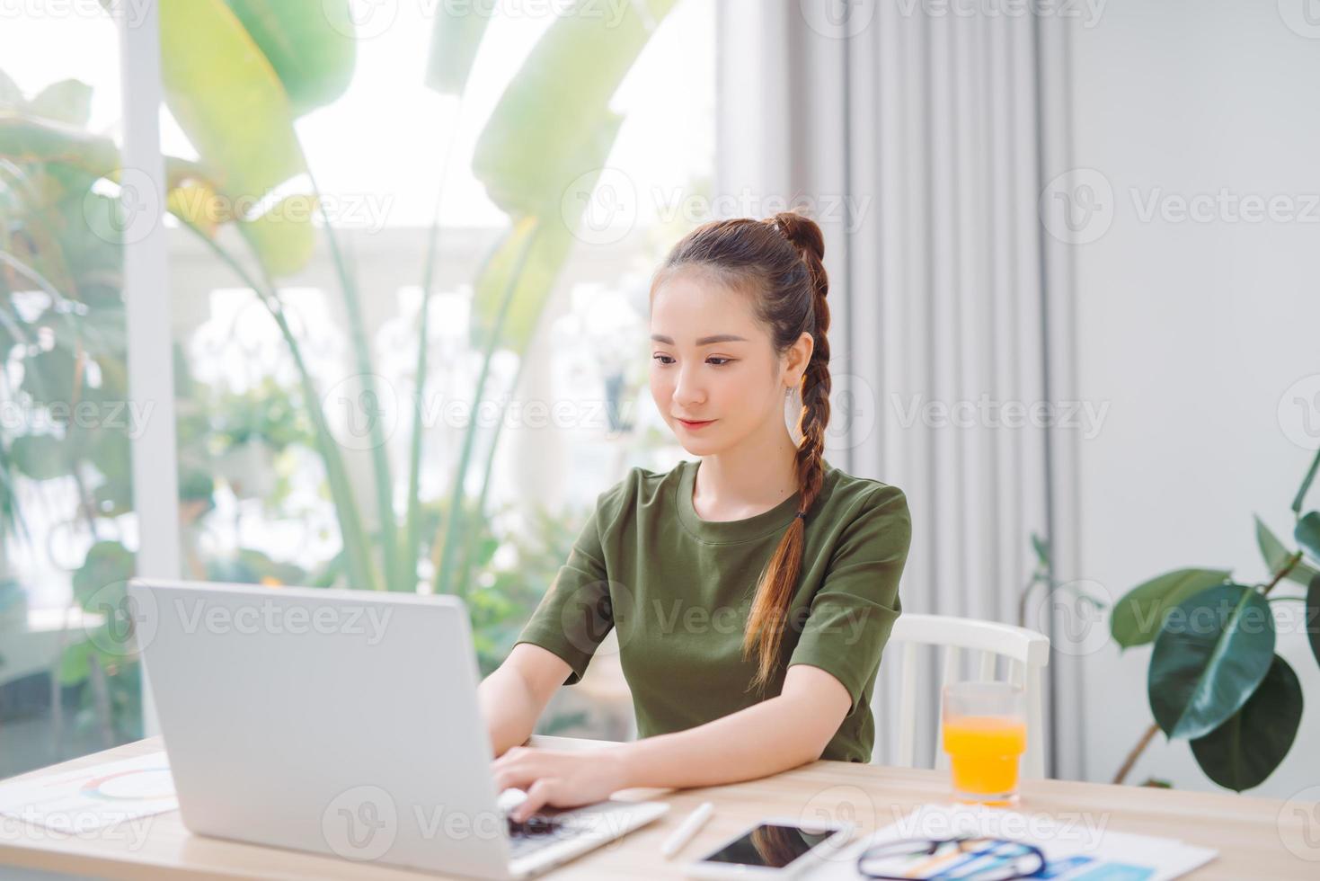 hübsche asiatische frau, die e-mail auf laptop schreibt, während sie zu hause sitzt foto