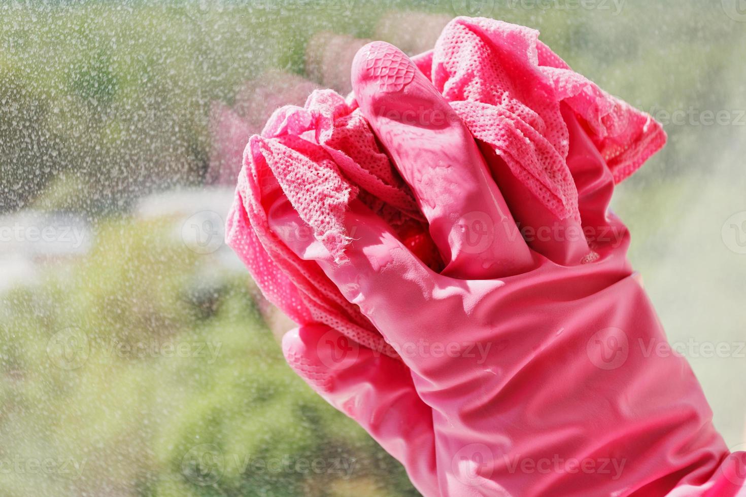 Hand in rosafarbenem Handschuh, der Fensterglas wäscht foto