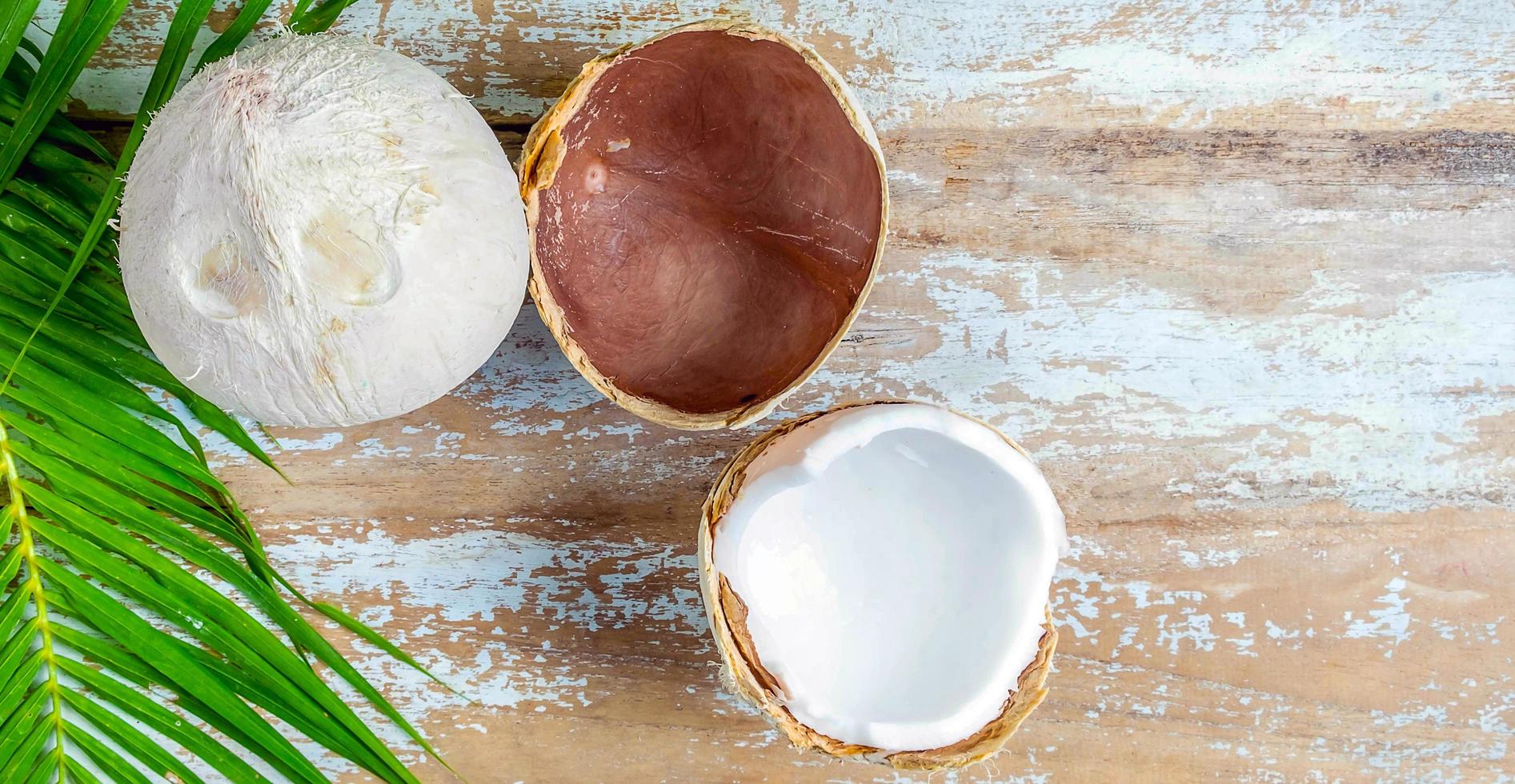 Eine frische Kokosnuss mit halbierten Schalen, die weißes Kokosnussfleisch und Kokosnussblätter auf einem alten Holzhintergrund enthüllt. foto