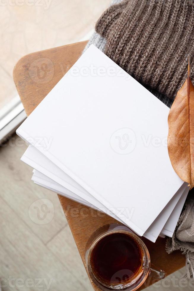 Stapel weißer leerer Bücher mit Herbstlaub und einer Tasse heißen Tees auf altem Holzstuhl, Mockup-Design foto