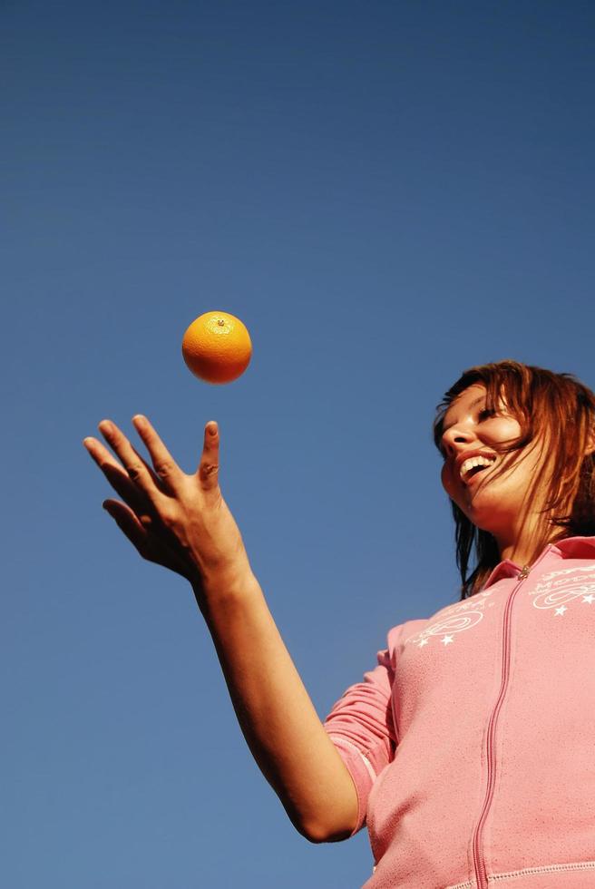 schönes Mädchen, das Orange in die Luft wirft foto