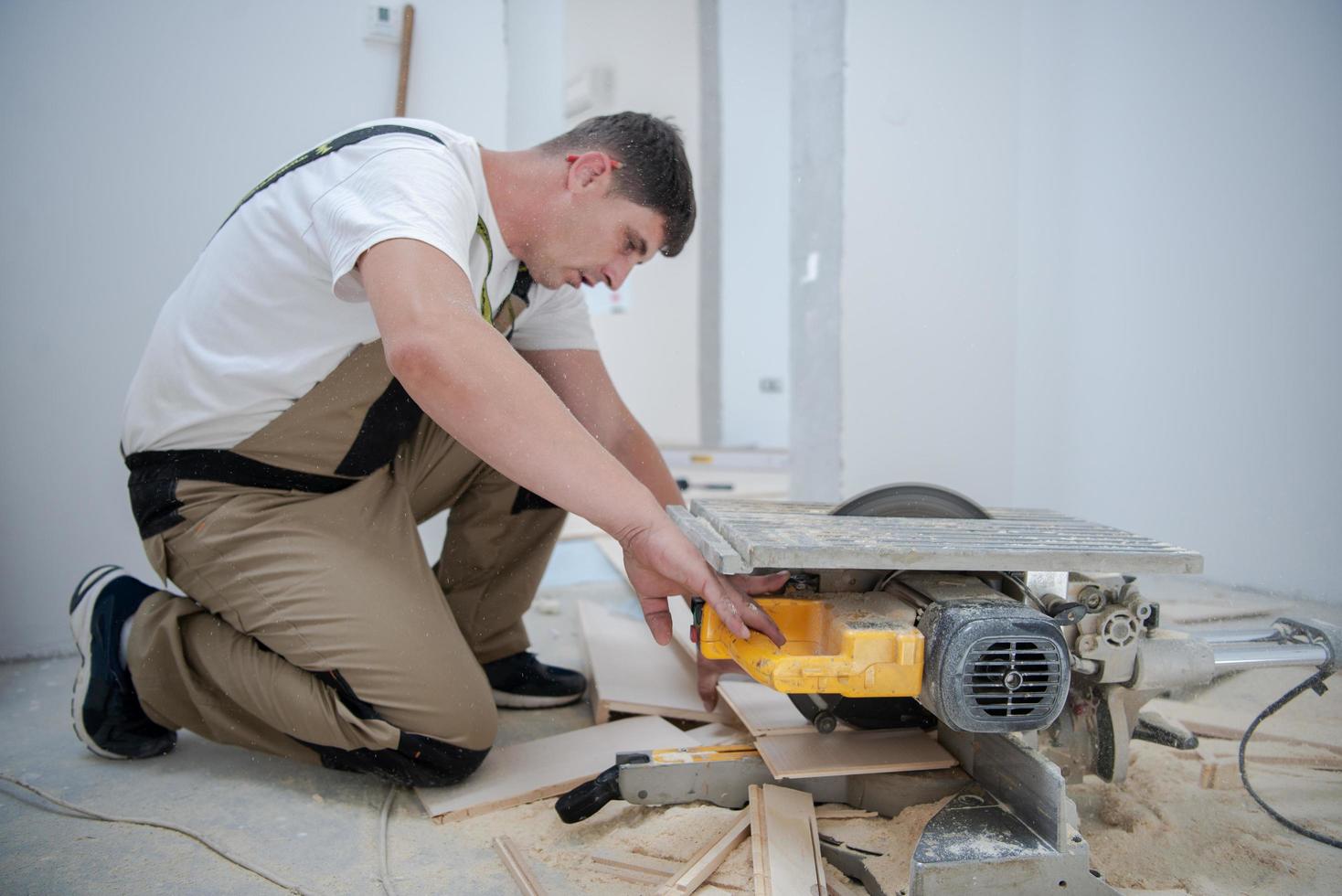 Mann schneidet Laminatdiele mit elektrischer Kreissäge foto