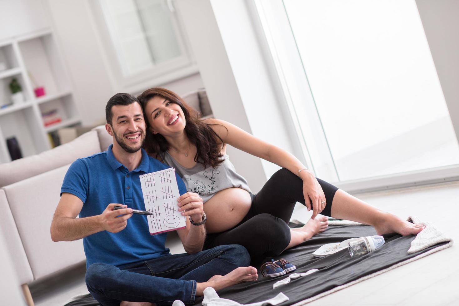 schwangeres paar, das eine liste von dingen für ihr ungeborenes baby überprüft foto