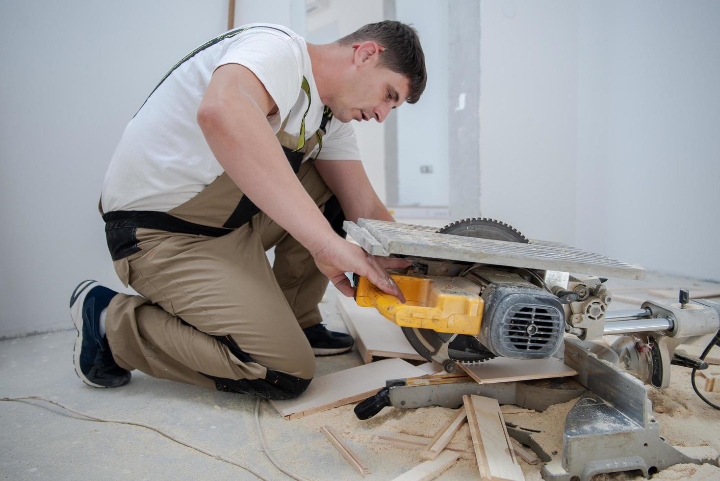 Mann schneidet Laminatdiele mit elektrischer Kreissäge foto