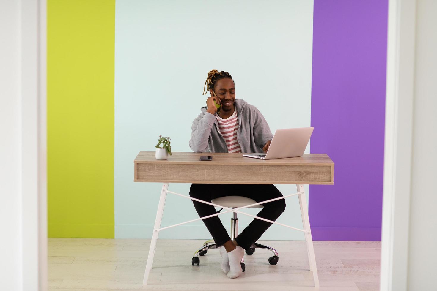 afro-junger mann sitzt während einer pandemie in seinem heimbüro und benutzt das telefon foto