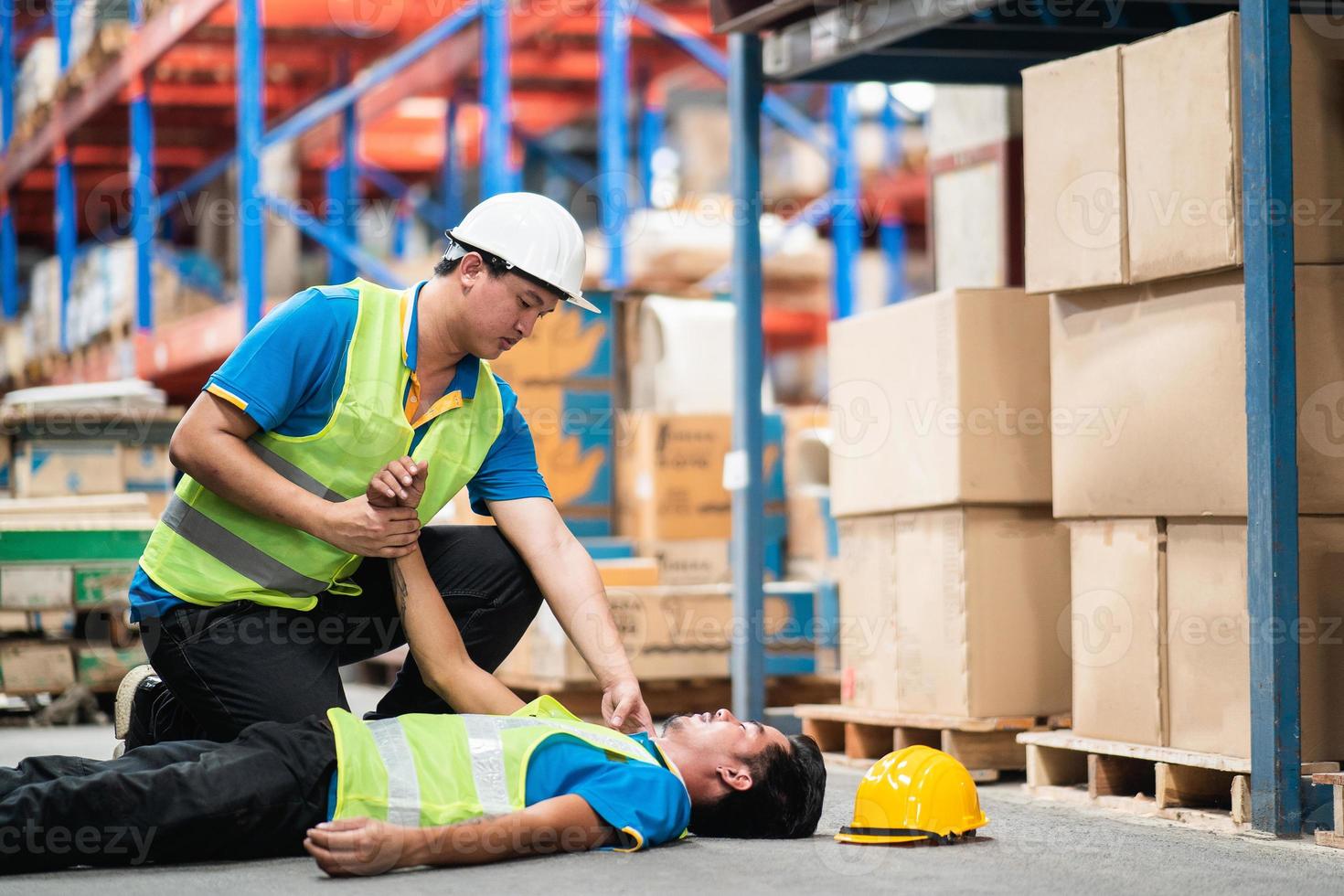 lagerarbeiter hat arbeitsunfall mitarbeiter schließen sich zusammen helfen erste hilfe zu leisten, um sie zu schützen. während die Mitarbeiter im Werkslager Regalbestände überprüfen. Industrielles Lagerkonzept. foto