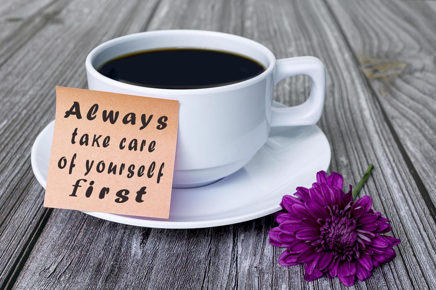 Motivationszitat geschrieben auf Haftnotiz mit weißer Kaffeetasse und lila Blume foto