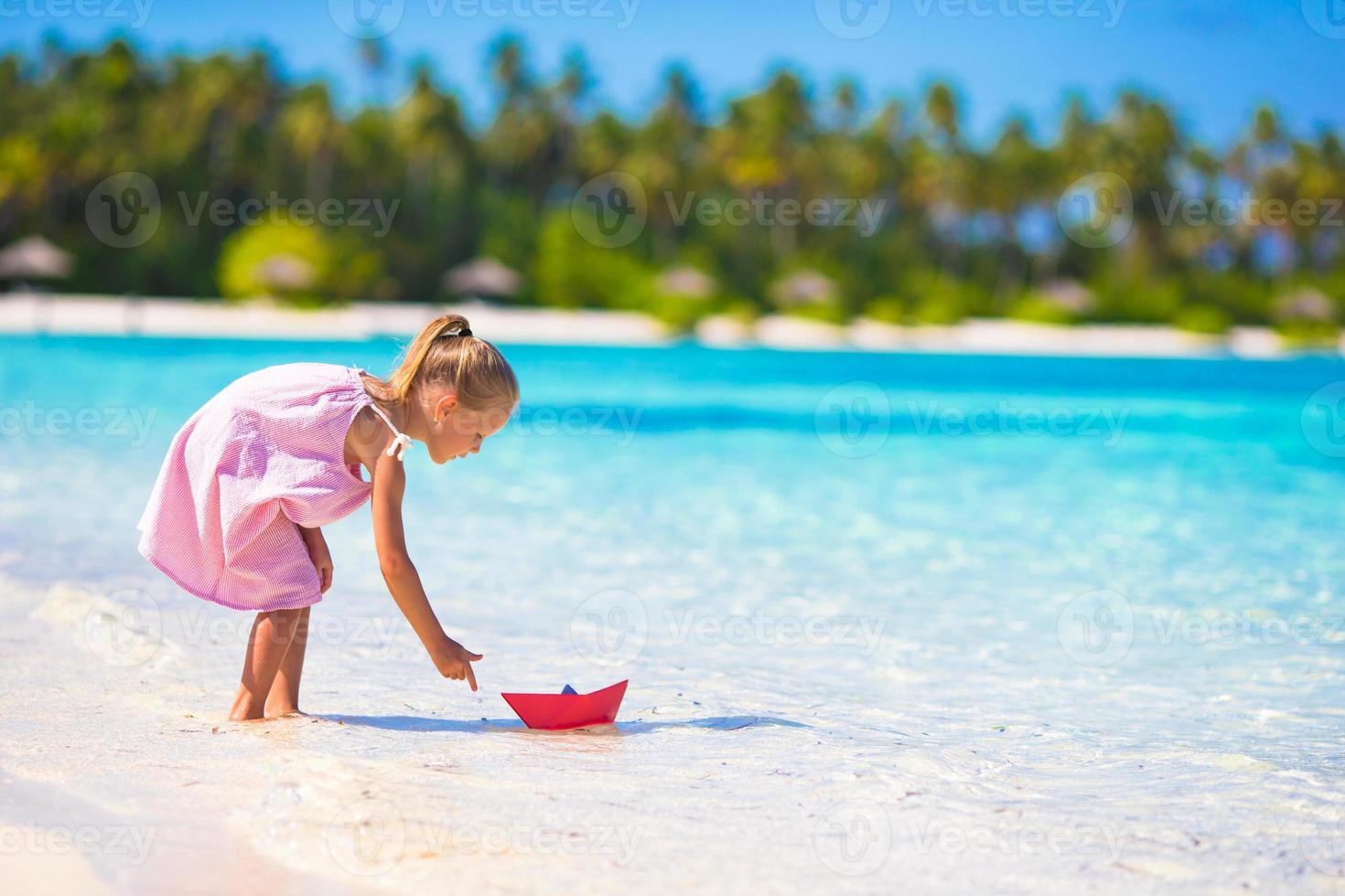 entzückendes kleines mädchen, das mit origami-boot im türkisfarbenen meer spielt foto