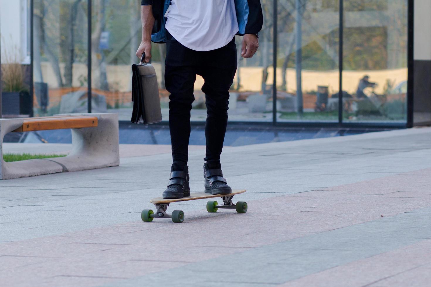 Konzept des jungen, schnellen und mobilen Managers. lustiger buisinessman auf skateboard im schwarzen anzug. foto