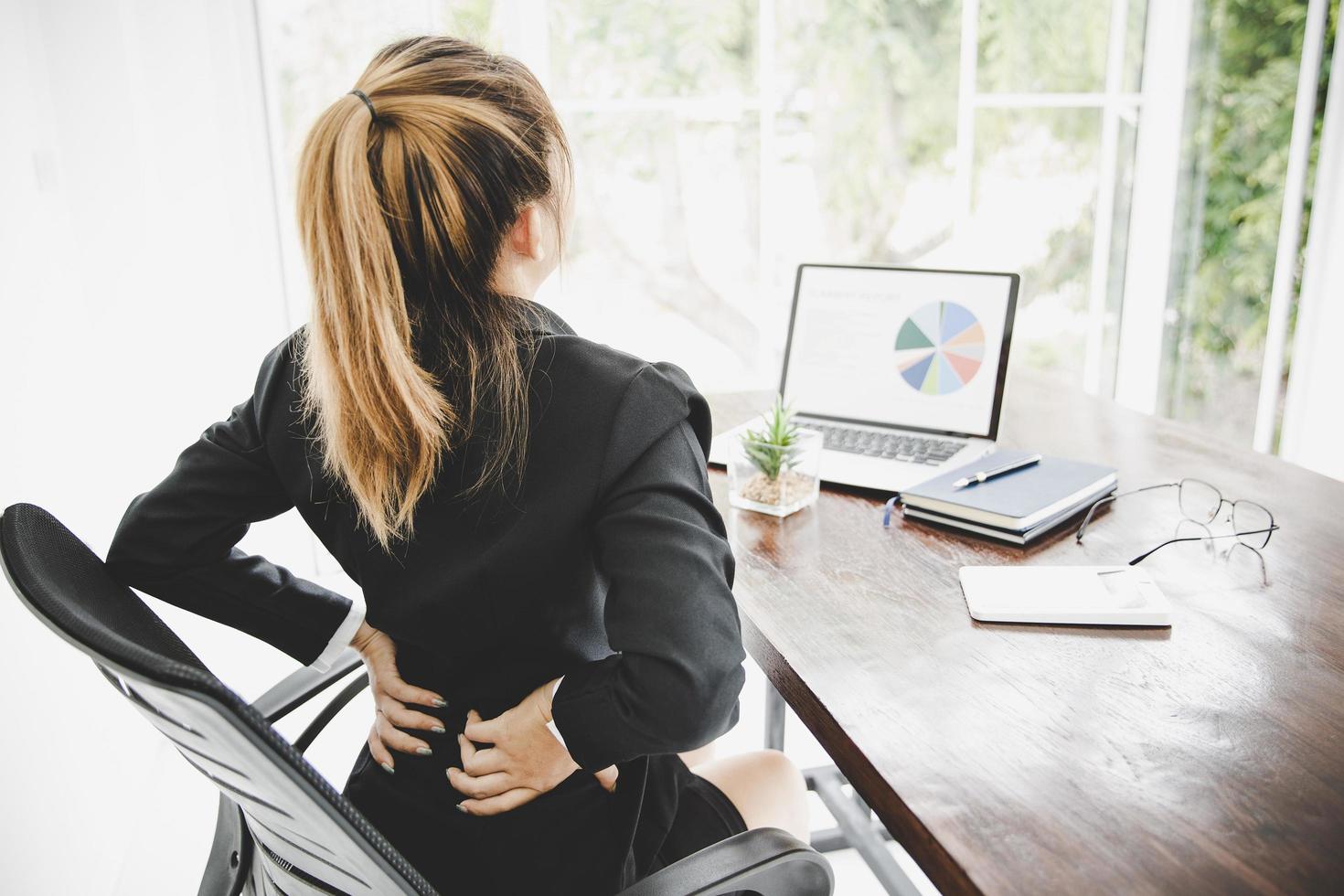 junge Geschäftsfrau im Büro mit schrecklichen Rückenschmerzen foto