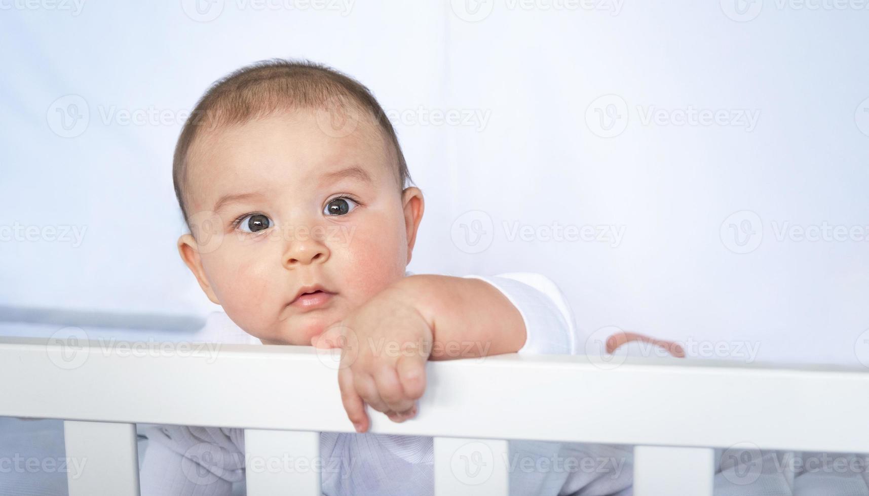 süßes Porträt eines Babys in einer Krippe aus nächster Nähe. ein Kind in weißer Kleidung auf weißer Unterwäsche. Zärtlichkeit und Fürsorge, Kinderprobleme. foto