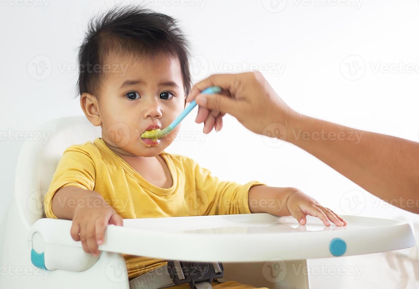 süßes weißes Mädchen sitzender Stuhl beim Frühstück im Innenbereich, der köstliche Mahlzeiten füttert, die sehr nahrhaft sind. Das Baby hat ein fröhliches Gesicht, lustig lächelnd und glücklich in einem gesunden Familienlebensstil. foto