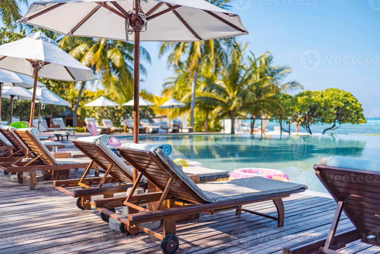 Sonnenschirme und Stühle rund um den Außenpool im Resorthotel für den Freizeit-Lifestyle im Urlaub. Luxus-Destination-Konzept, Lounge-Nahaufnahme unter Palmen, Entspannung, ruhige Atmosphäre foto