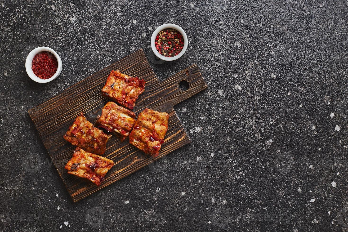 Appetitlich gebackene Schweinerippchen mit Pfeffer und Paprika auf Holzbrett auf dunklem Hintergrund. amerikanisches lebensmittelkonzept. Draufsicht, Kopierbereich. foto