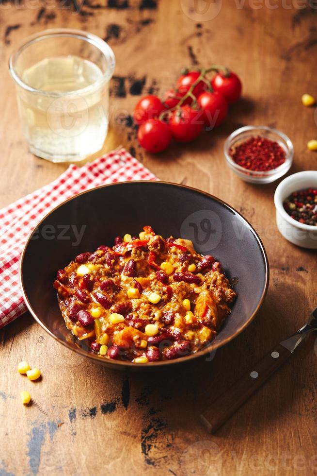 Chili con Carne mit Hackfleisch, Bohnen und Mais in dunkler Schüssel auf Holzhintergrund. mexikanische und texanische küche foto