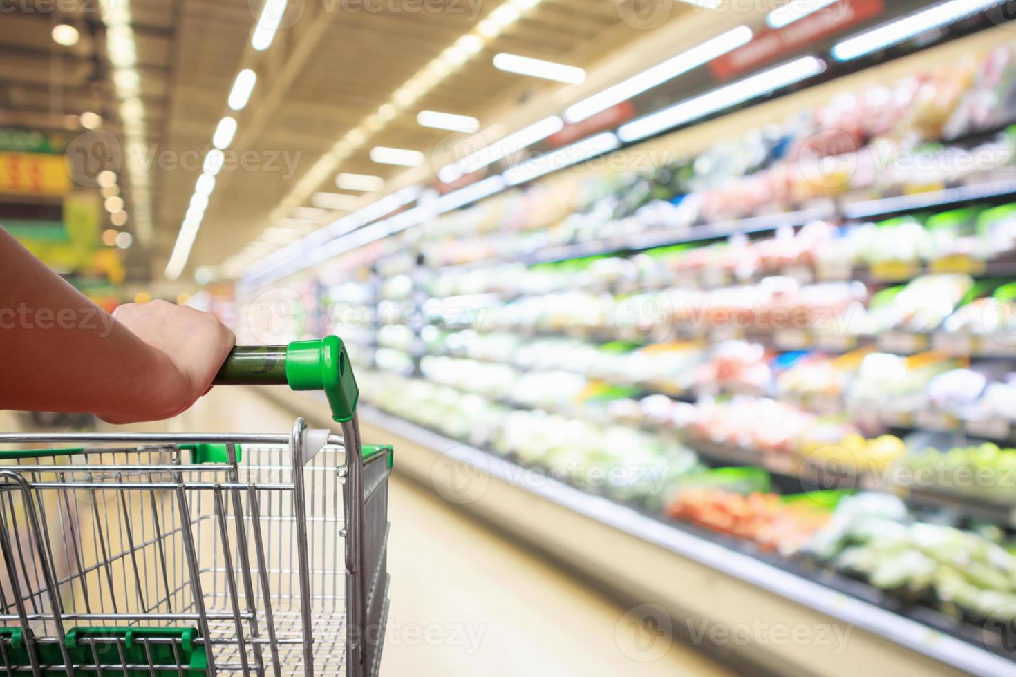 Frau hält Supermarkt-Einkaufswagen mit abstrakter Unschärfe organisches frisches Obst und Gemüse in den Regalen im Lebensmittelgeschäft foto