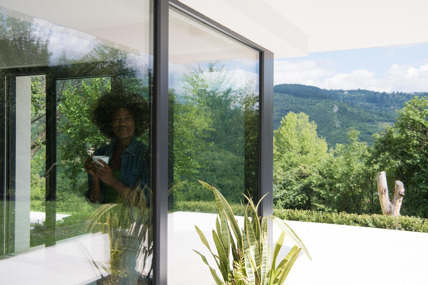 Afroamerikanerin trinkt Kaffee und schaut aus dem Fenster foto