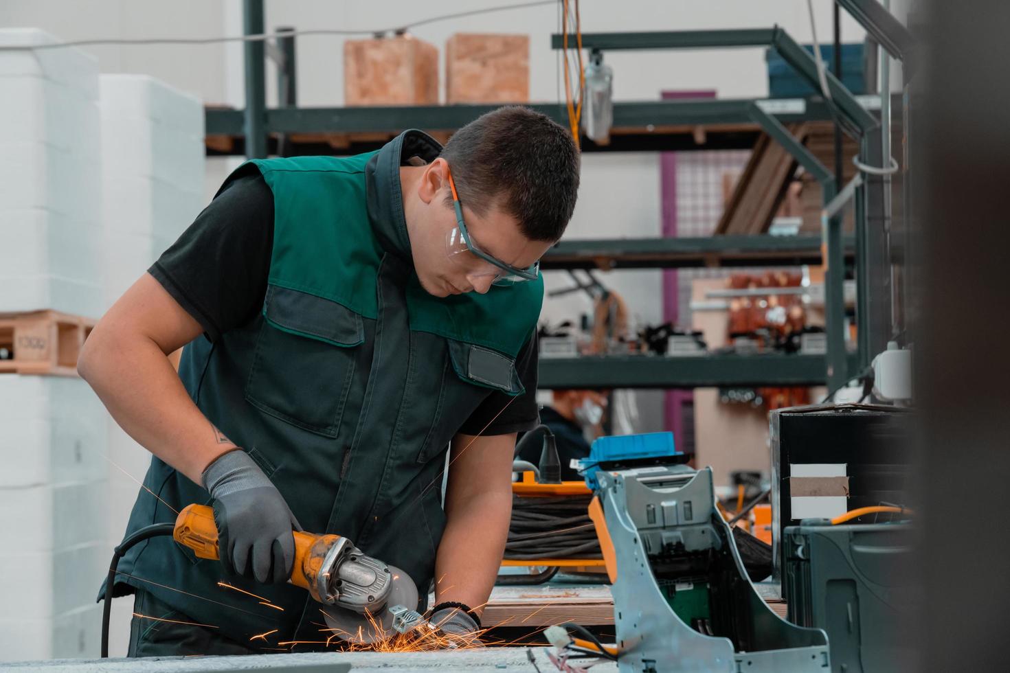 schwerindustrie-fabrikinnenraum mit industriearbeiter, der winkelschleifer verwendet und ein metallrohr schneidet. Auftragnehmer in der Herstellung von Metallstrukturen für Sicherheitsuniformen und Schutzhelme. foto